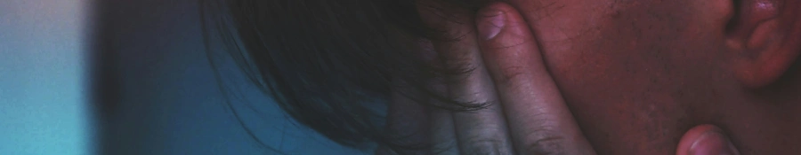 Mand som sidder i et dunket lokale med hænderne foran ansigtet